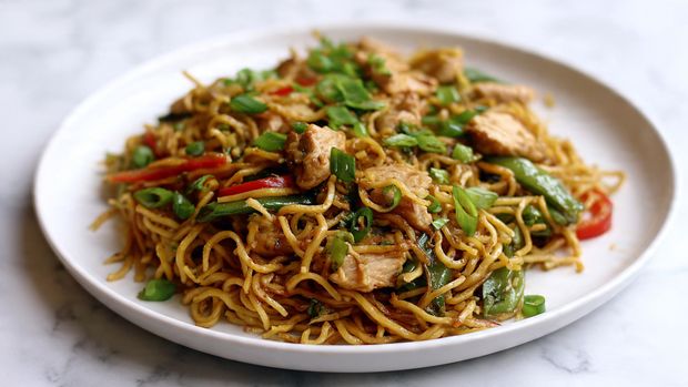 Chicken Ramen Stir Fry Recipe 5 A white plate holds a serving of stir-fried noodles mixed with pieces of cooked chicken, green snow peas, and thin slices of red bell pepper. The noodles are golden-brown with a slightly shiny texture, resting beneath scattered bright green chopped scallions that add a fresh pop of color on top. The chicken pieces are lightly browned and scattered evenly through the dish. The plate is placed on a white marbled surface, creating a clean, bright background. photo taken with an iphone --ar 4:5 --v 7