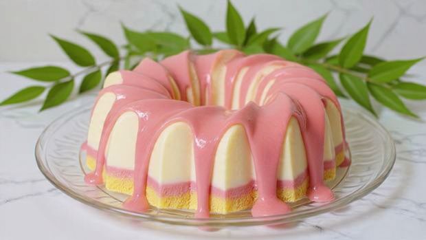 The image shows a ring-shaped yellow cake with two thick layers of glaze pouring over the sides. The top layer glaze is bright pink, covering most of the cake and flowing down unevenly. Underneath the pink, bright yellow glaze peeks out in thick drips, creating a colorful contrast on the ring. The cake sits on a clear glass plate placed on a white marbled surface. In the background, there are three metal containers. The photo is taken with an iphone --ar 4:5 --v 7
