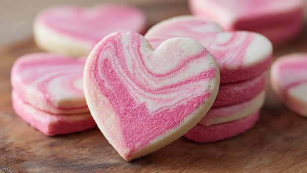 The image shows smooth dough balls in two colors, cream and bright pink, arranged in rows on a white marbled textured surface. Each dough ball is round with a slightly shiny and soft texture, alternating in color between cream and pink. The dough balls are closely placed but not touching, and the focus is on the middle section with some dough balls blurred in the background and foreground. The white marbled texture underneath adds a clean, simple look to the setup. photo taken with an iphone --ar 4:5 --v 7